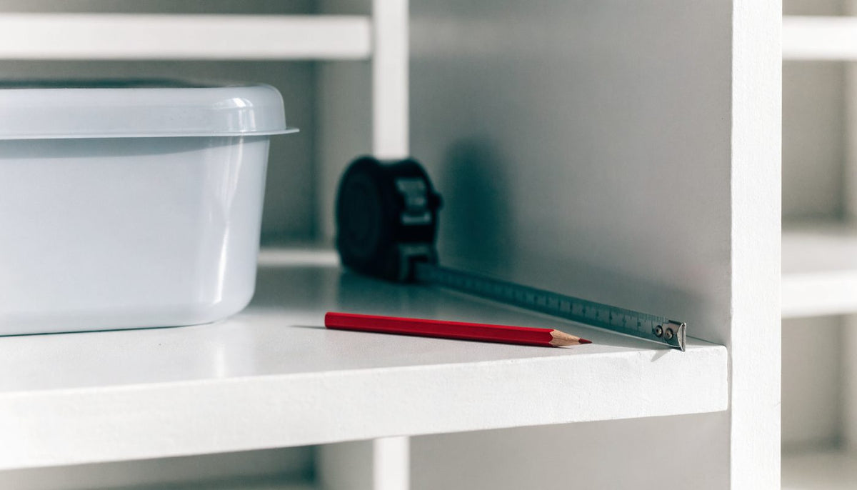 A tape measure and a storage bin on a white cabinet shelf