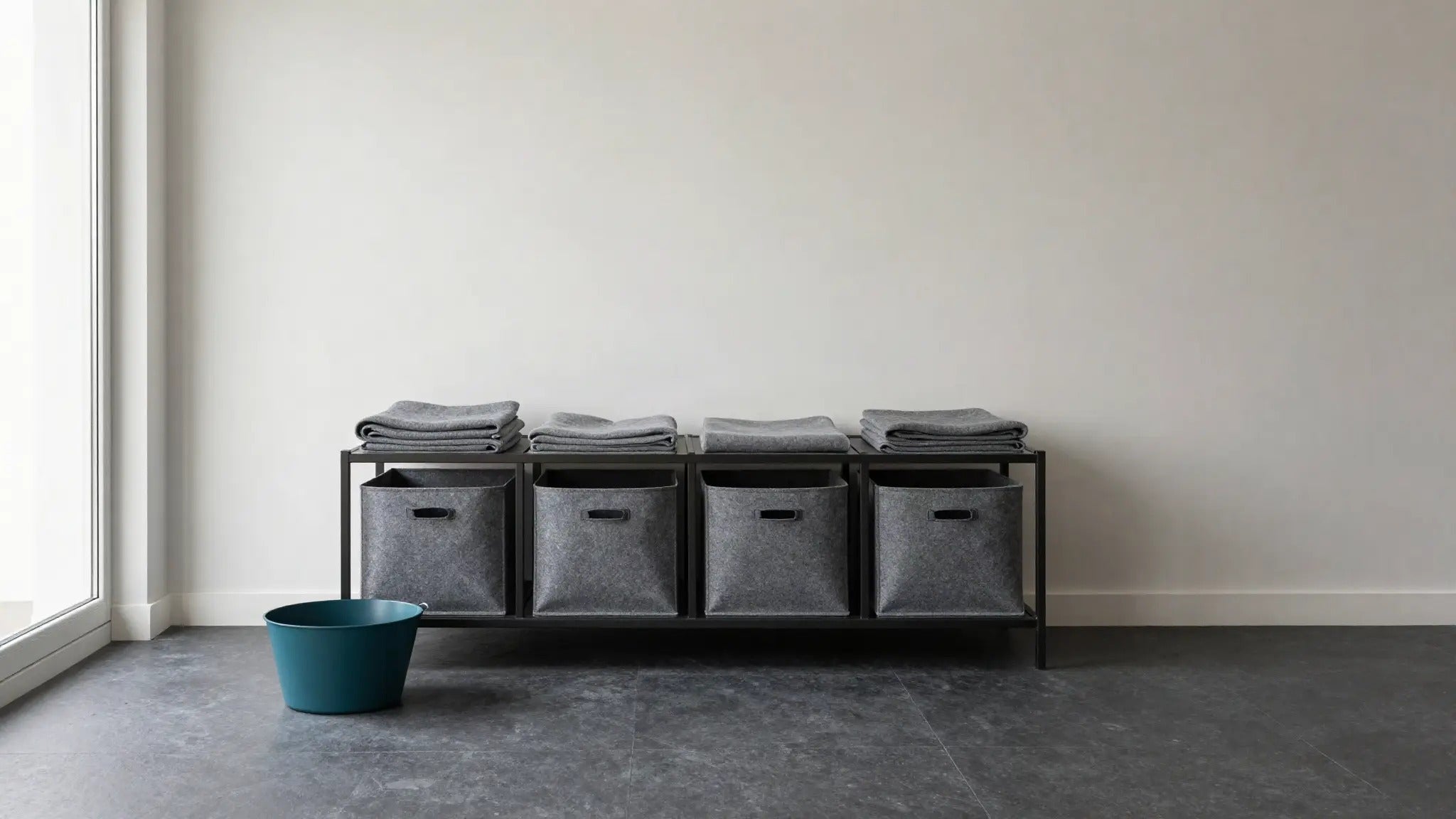 Low shelf unit with grey felt storage bins and folded blankets